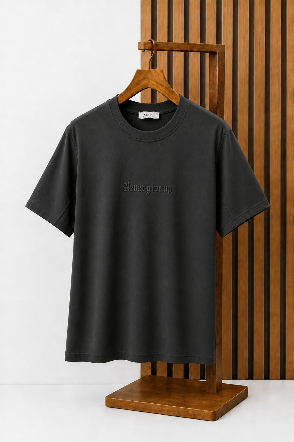 Never Give Up Embroidered Tee in Charcoal, on a wooden hanger