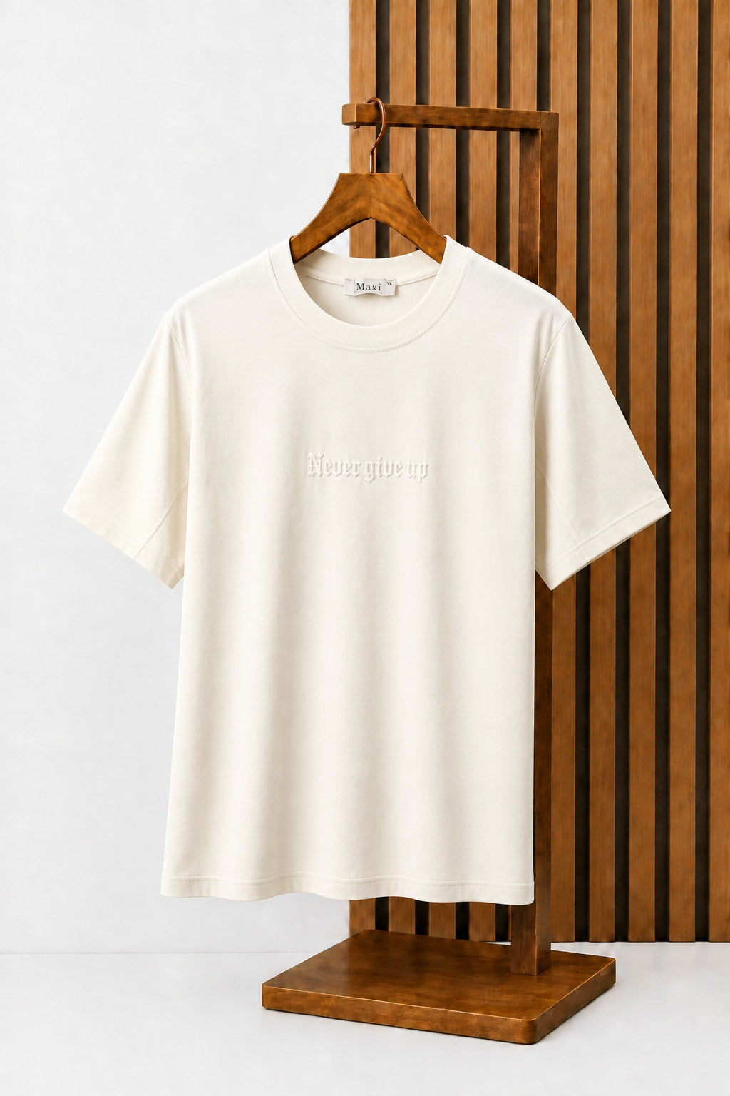 Never Give Up Embroidered Tee in Ecru, on a wooden hanger